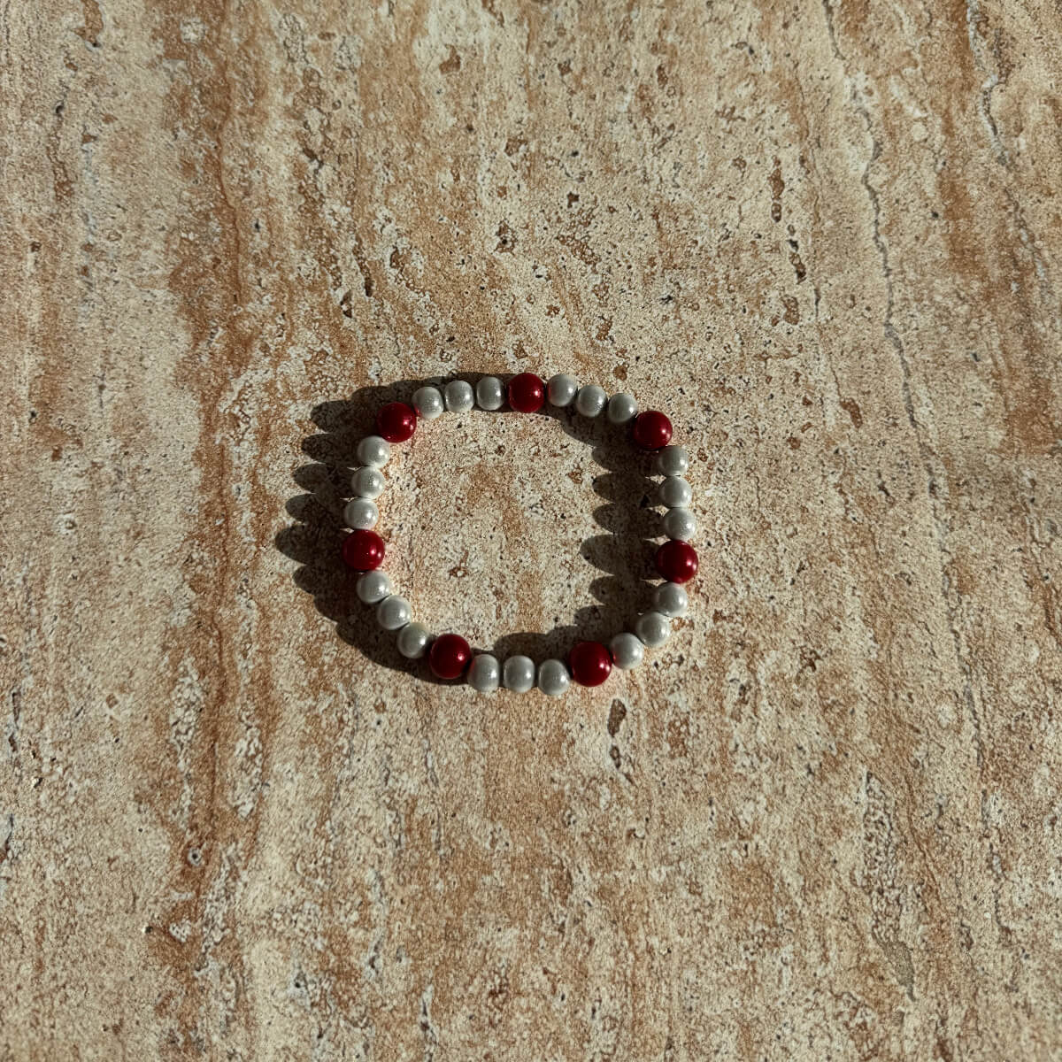 Armband aus hellgrauen Perlen mit roten Akzenten liegt stilvoll auf einer cremefarbenen Schale.