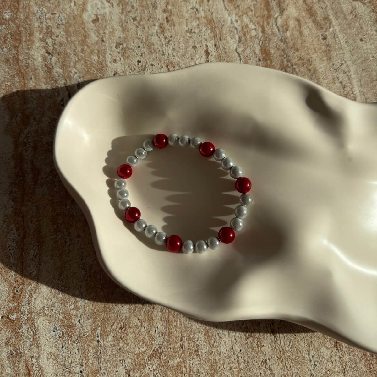 Nahaufnahme des grauen Armbands mit roten Perlen in einer eleganten Schale im Licht.