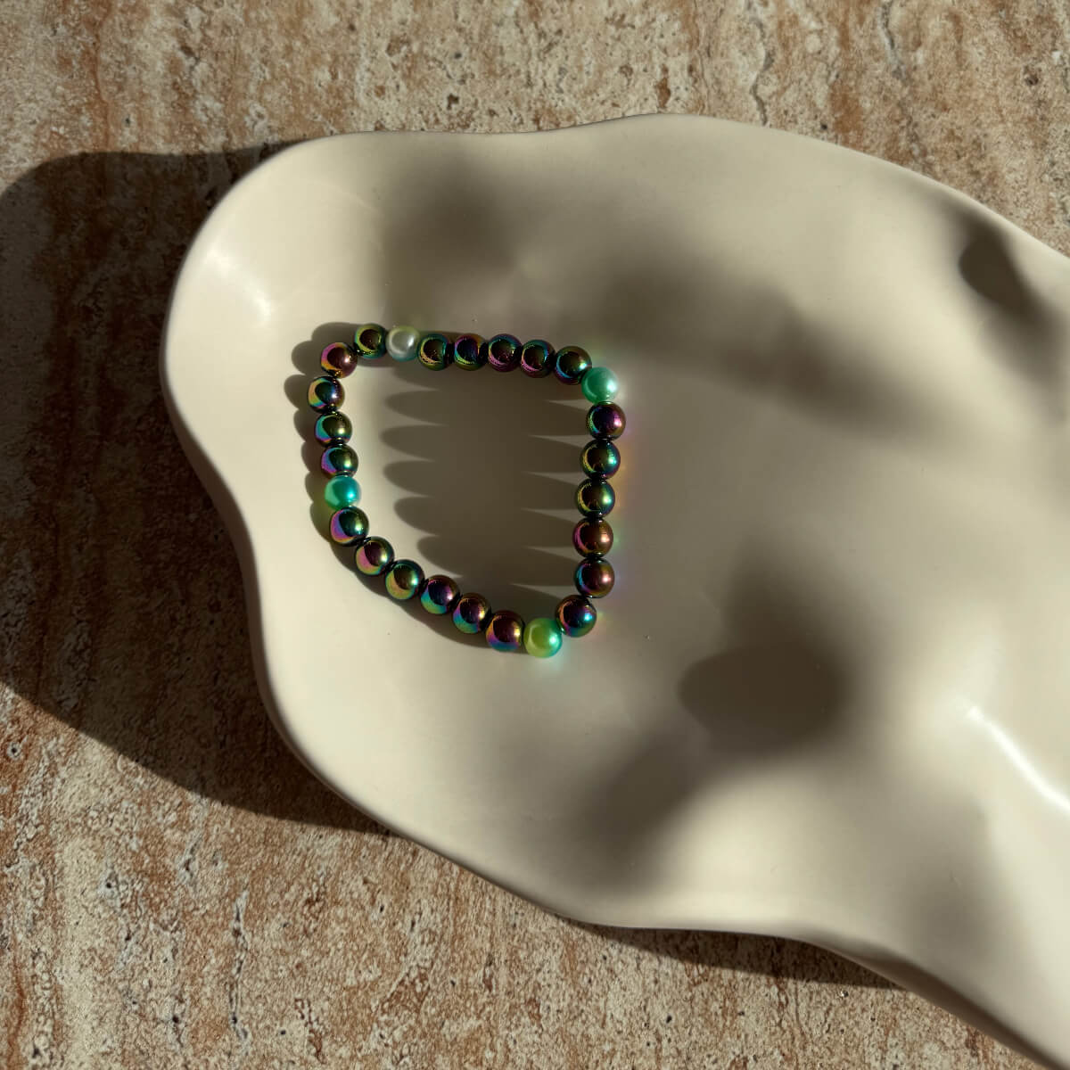 Nahaufnahme des Aurora Glow Armbands in einer cremefarbenen Schale mit reflektierendem Glanz.