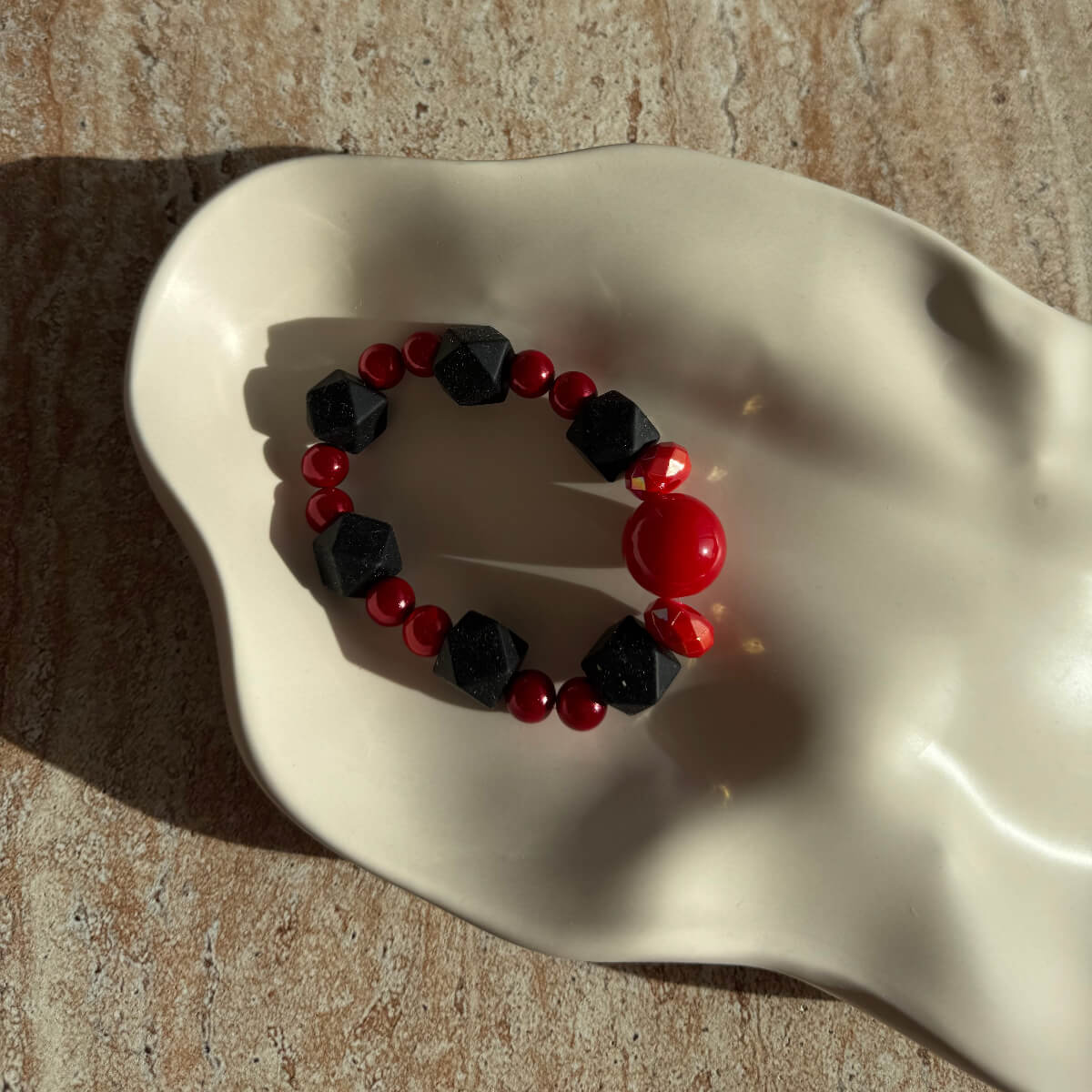 Nahaufnahme des Crimson Shadows Armbands in einer Schale, im warmen Sonnenlicht.