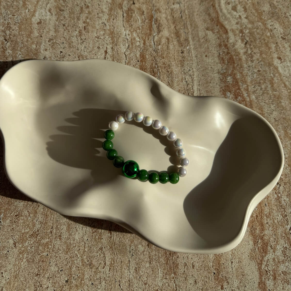 Das vollständige Emerald Pearl Harmony Armband liegend in einer cremefarbenen Schale, weich ausgeleuchtet.