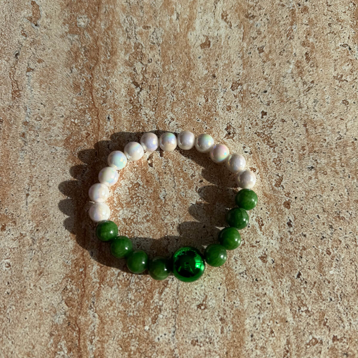 Armband Emerald Pearl Harmony auf hellem Untergrund, aufgenommen auf einem Tisch bei natürlichem Licht.