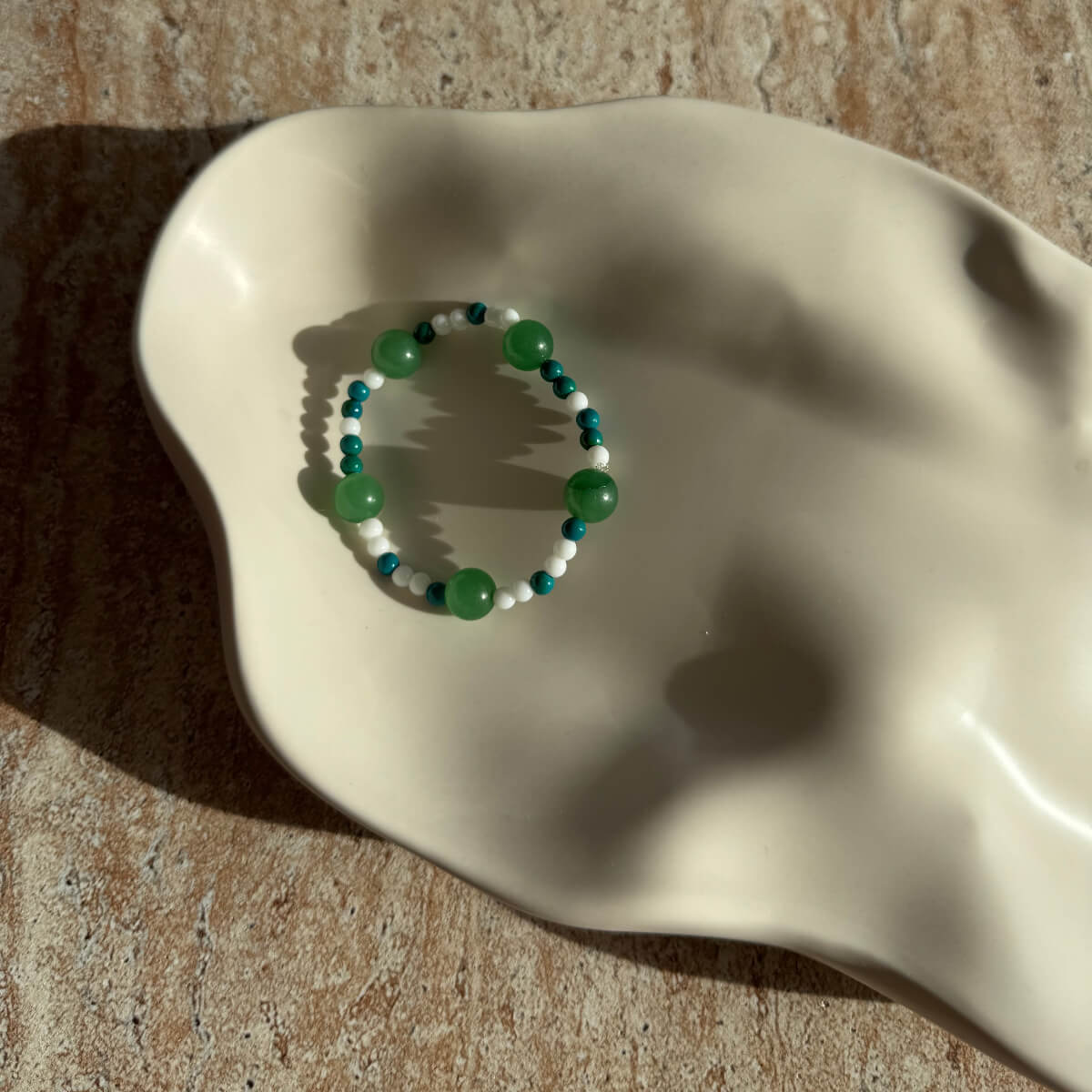 Nahaufnahme des Emerald Tide Armbands mit schimmernden Grüntönen in einer dekorativen Schale.