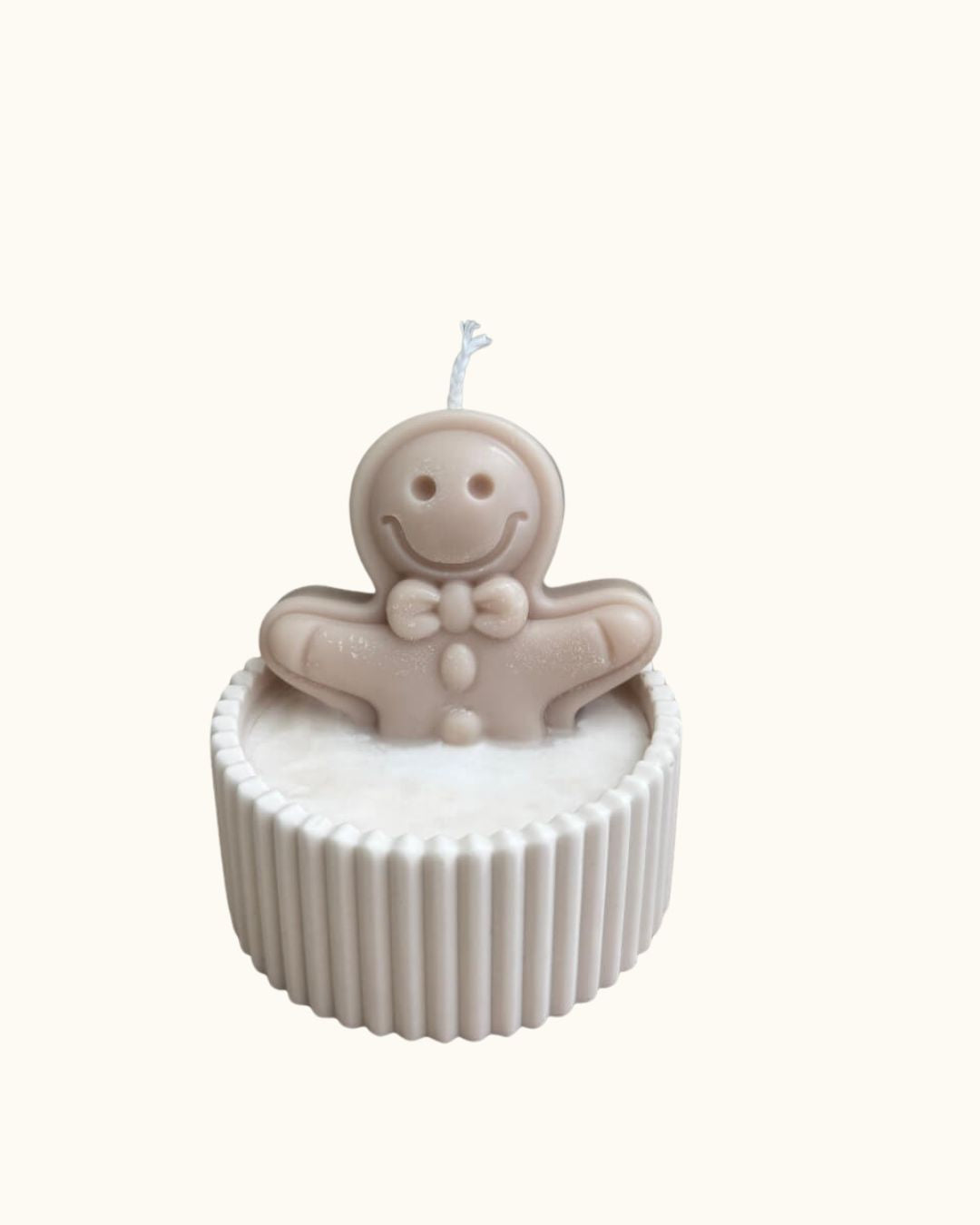 Handgegossene Weihnachtskerze in runder Schale auf einem Holztisch, mit schneeweißem Wachsboden und liebevollen Lebkuchen-Details aus Wachs.