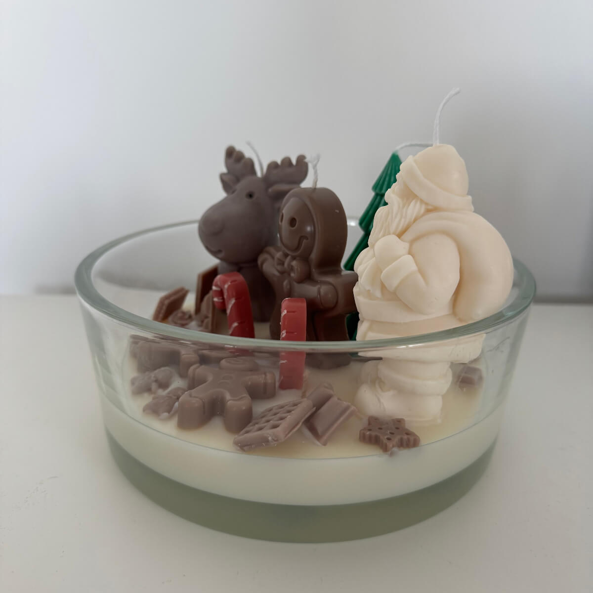 Obenansicht der Schalenkerze mit Tannenbaum, Schneemann und bunten Süßigkeiten auf schneeweißem Wachs.