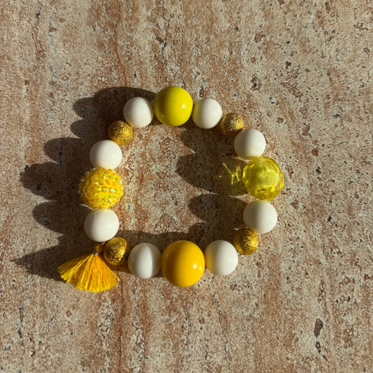 Gelb-weißes Armband Sunny Sorbet auf einem Tisch, handgefertigt von Sym Aesthetics.