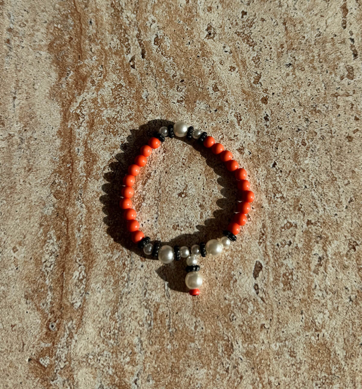 Handgefertigtes Armband aus orangefarbenen, weißen und schwarzen Perlen, präsentiert auf einer cremefarbenen Schale – minimalistisches Aesthetic Design mit edlem Glanz.