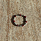 Armband aus hellgrauen Perlen mit roten Akzenten liegt stilvoll auf einer cremefarbenen Schale.