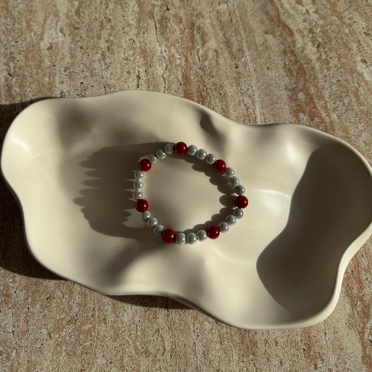 Komplette Ansicht des hellgrauen Armbands mit roten Details in einer hellen Schale präsentiert.