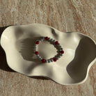 Komplette Ansicht des hellgrauen Armbands mit roten Details in einer hellen Schale präsentiert.