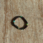 Armband mit schimmernden, mehrfarbigen Perlen auf einem beigen Dekoteller im Sonnenlicht.