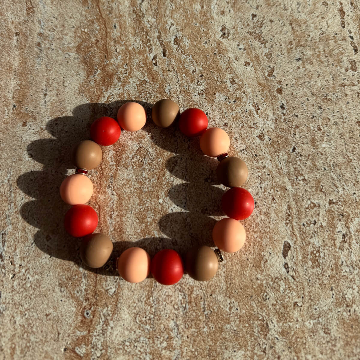 Armband Caramel Ember aus roten, nude und caramel-farbenen Perlen – fotografiert auf einem Tisch.
