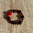 Schwarzes und rotes Armband mit facettierten Perlen, auf einem Tisch arrangiert.