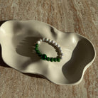 Das vollständige Emerald Pearl Harmony Armband liegend in einer cremefarbenen Schale, weich ausgeleuchtet.