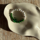 Nahaufnahme des Emerald Pearl Harmony Armbands in einer Schale mit Fokus auf die grünen und weißen Perlen.