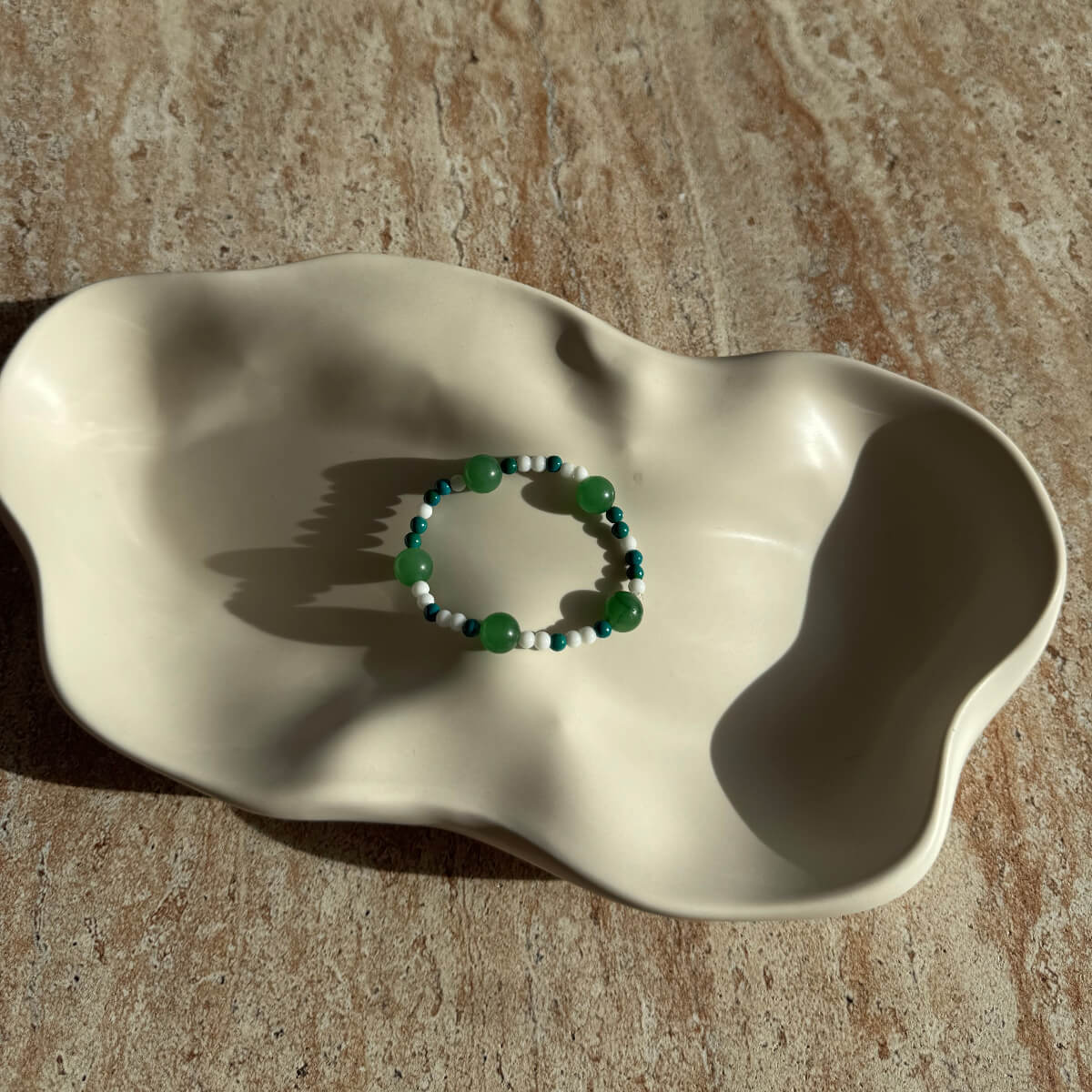 Komplettes Emerald Tide Armband in einer Schale, im Sonnenlicht auf einer natürlichen Steinoberfläche fotografiert.