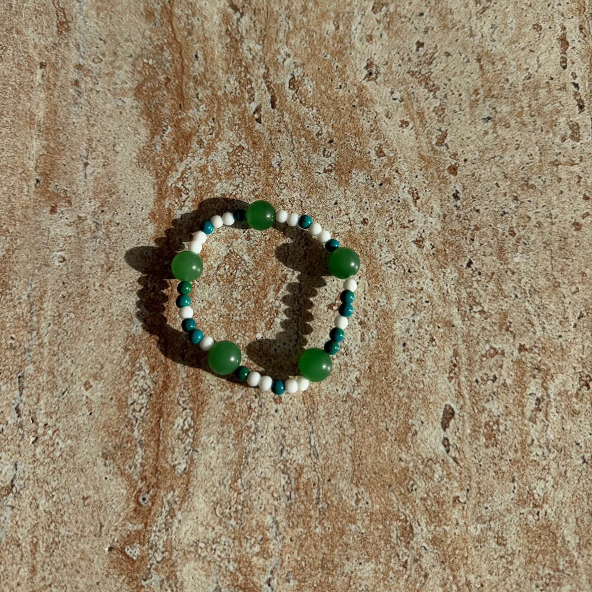 Handgefertigtes Armband mit grünen, weißen und türkisfarbenen Perlen auf einem cremefarbenen Untergrund.