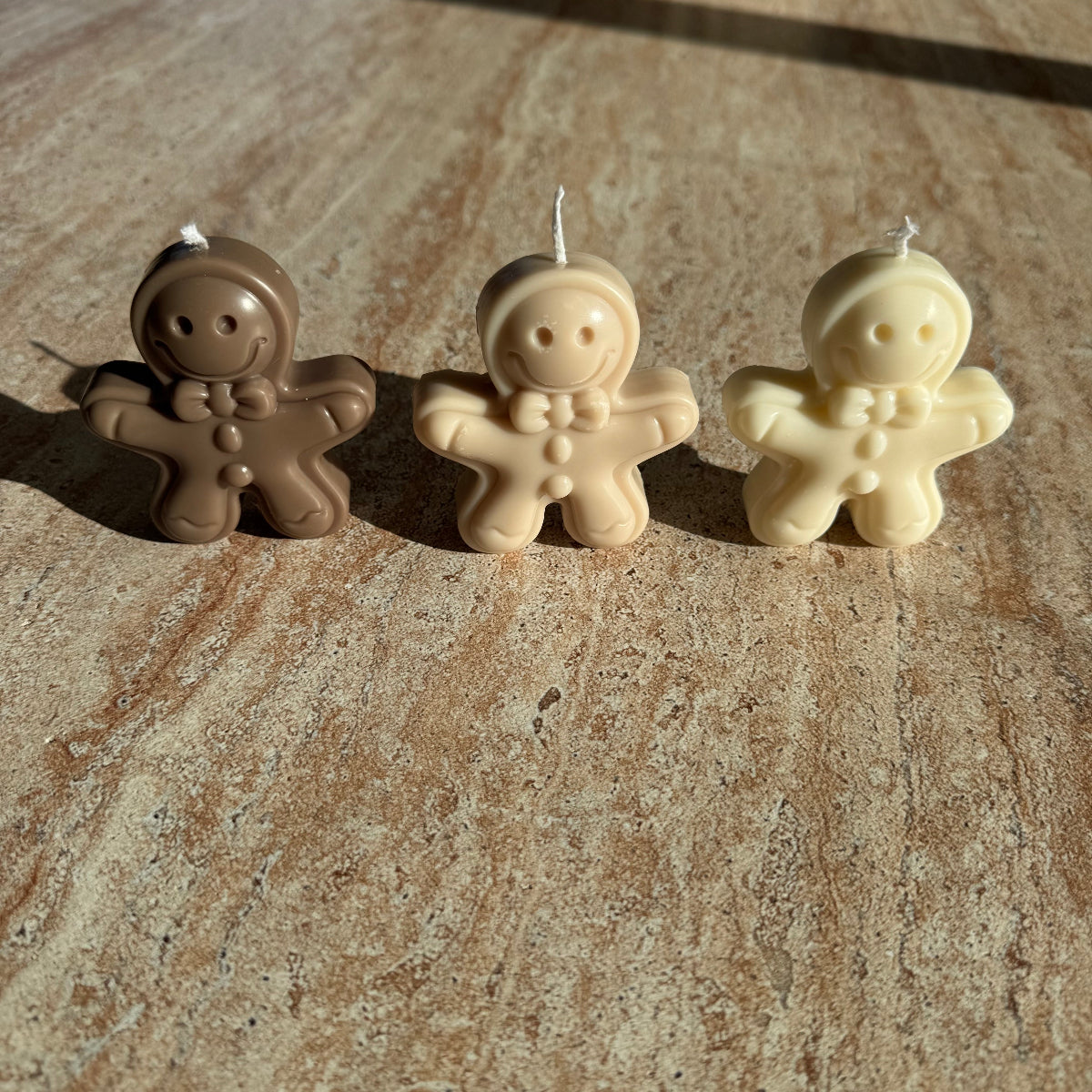 „Drei Gingerbread-Kerzen in verschiedenen Farben auf einem Tisch – Sym Aesthetics.“