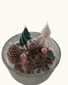 Handgegossene Weihnachtskerze in runder Schale auf einem Holztisch, mit schneeweißem Wachsboden und süßen Candy-Deko-Elementen inspiriert von Hänsel und Gretel.