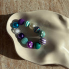 „Nahaufnahme des Mermaid Carnival Armbands in einer weißen Schale mit glitzernden und gestreiften Perlen.“