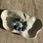 „Komplette Ansicht des Mermaid Carnival Armbands in der Schale, farbenfrohes Kugeldesign in Aqua und Lila.“