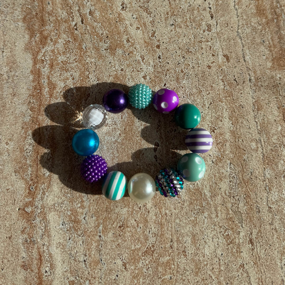 „Mermaid Carnival Armband mit bunten Aqua-, Türkis- und Lilaperlen auf einem Tisch arrangiert.“