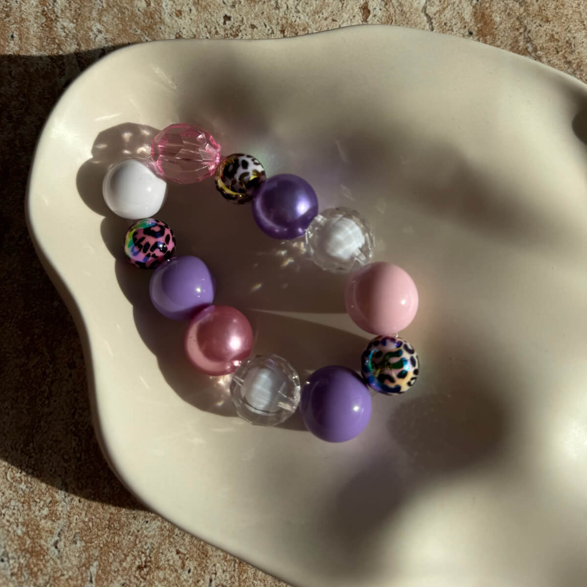 Nahaufnahme des Pastel Safari Armbands in einer Schale mit lila, rosa und gemusterten Perlen.