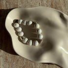 Nahaufnahme des Pearl Whisper Armbands in einer cremefarbenen Schale mit glänzenden Perlen.