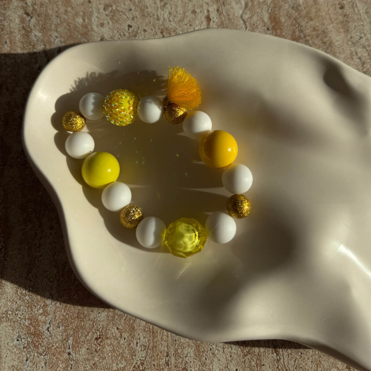 Nahaufnahme des Sunny-Sorbet-Armbands mit goldenen Details in einer cremefarbenen Schale.