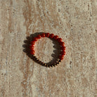 Armband aus orangefarbenen und bronzenen Perlen liegt auf einer cremefarbenen Schale im warmen Sonnenlicht.