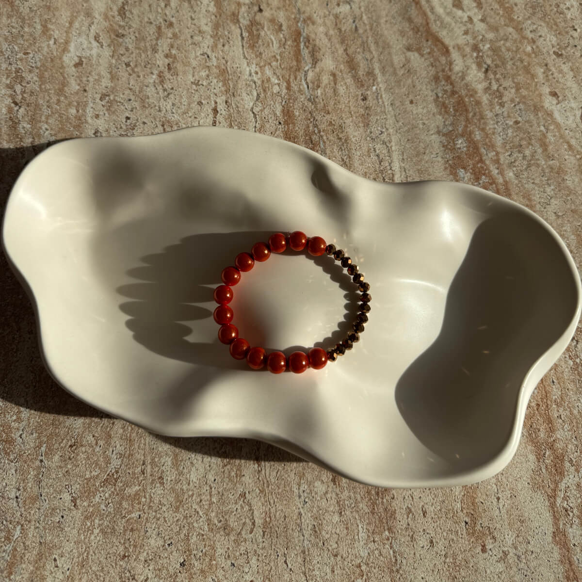 Komplette Ansicht des bronzefarbenen Armbands mit orangen Akzenten in einer hellen Schale.