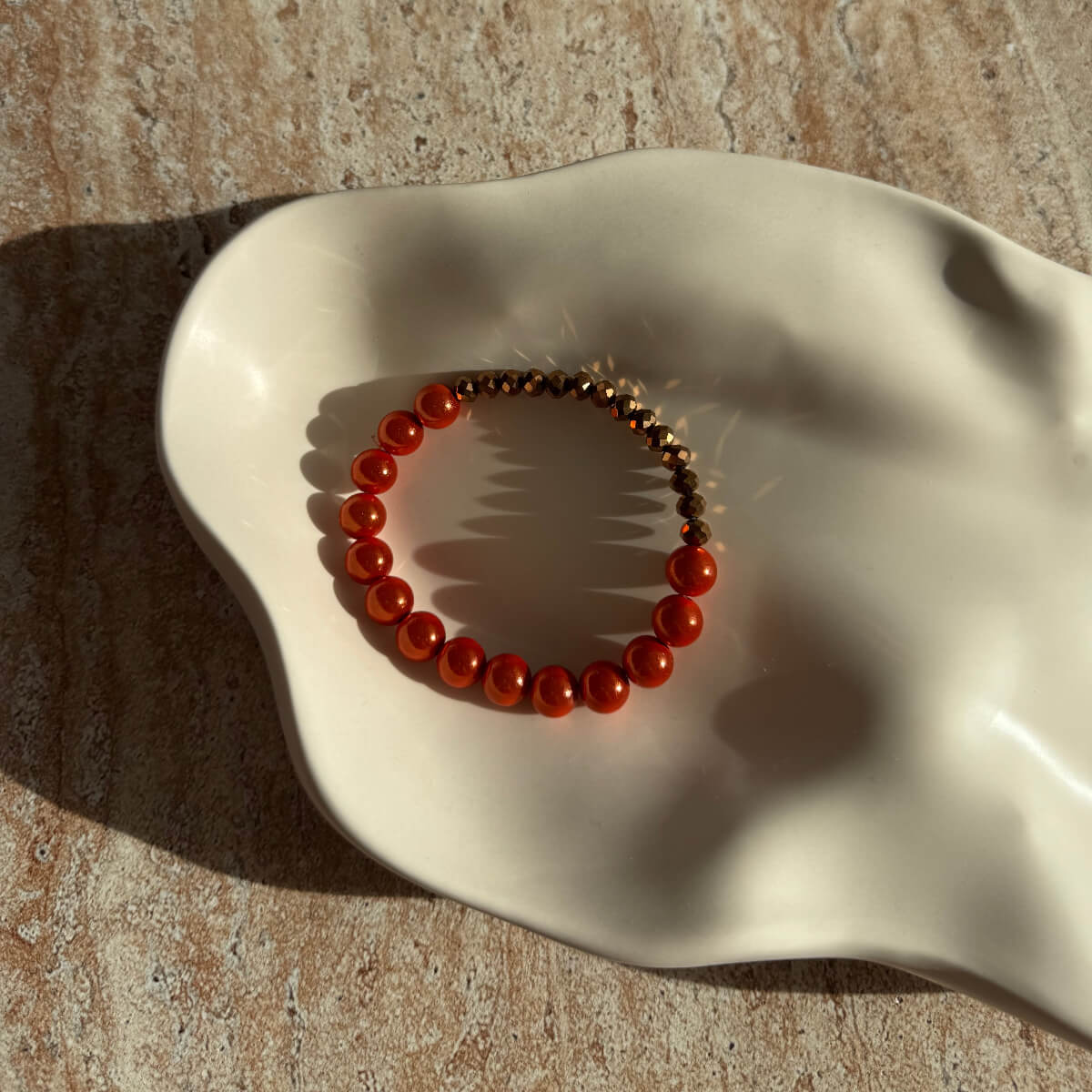 Nahaufnahme des orange-bronzenen Armbands in einer eleganten Schale mit feinem Glanz.