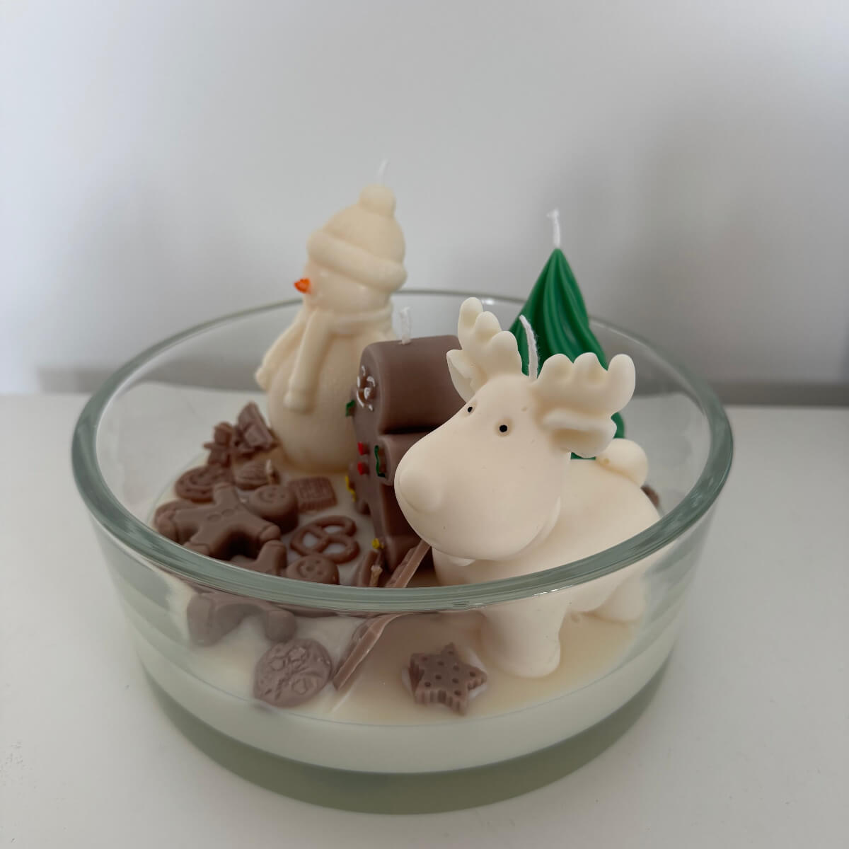 Nahaufnahme der liebevoll gestalteten Dekoration aus Wachs – Schneemann, Schokolade und Tannenbaum in weißem Schneewachs.