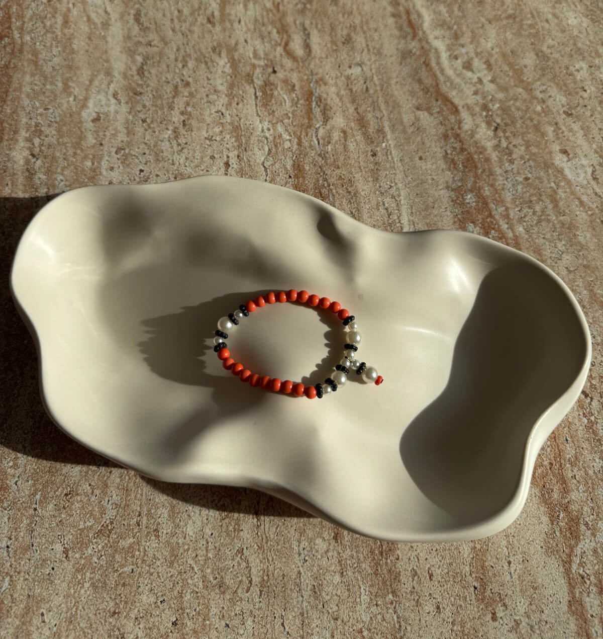 Nahaufnahme eines handgefertigten Armbands aus glänzenden Perlen in Orange, Weiß und Schwarz – elegantes Accessoire aus der Sym Aesthetics Kollektion.